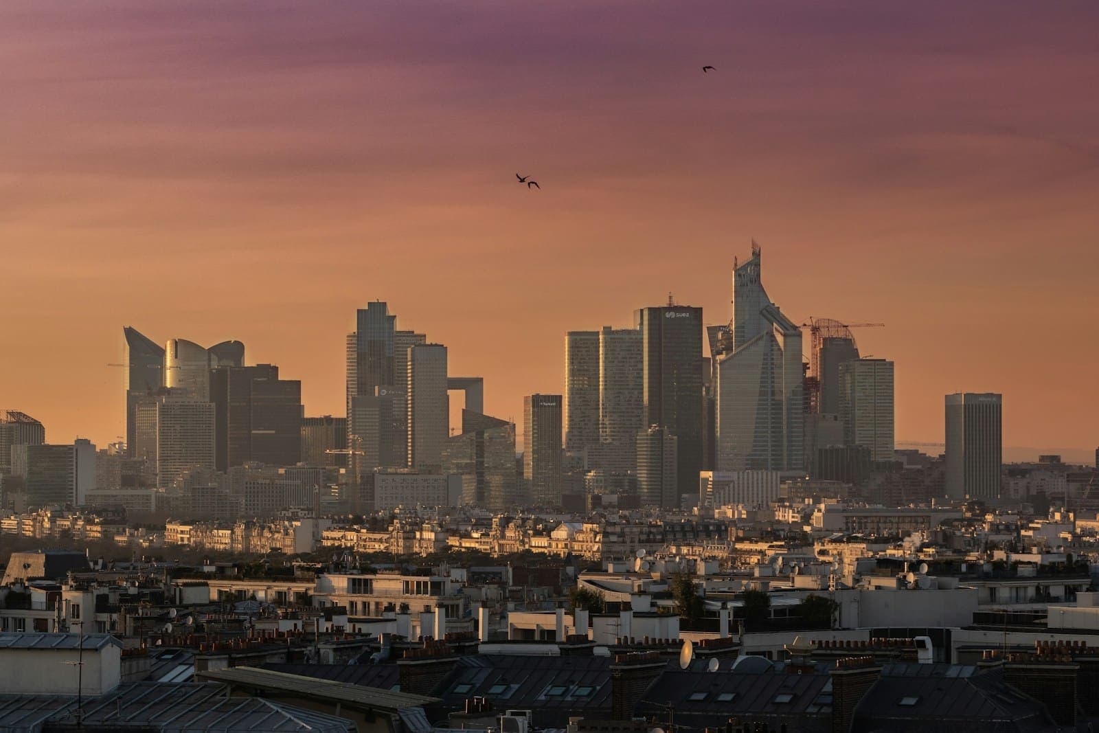 A city skyline glowing at golden hour on the horizon above European rooftops