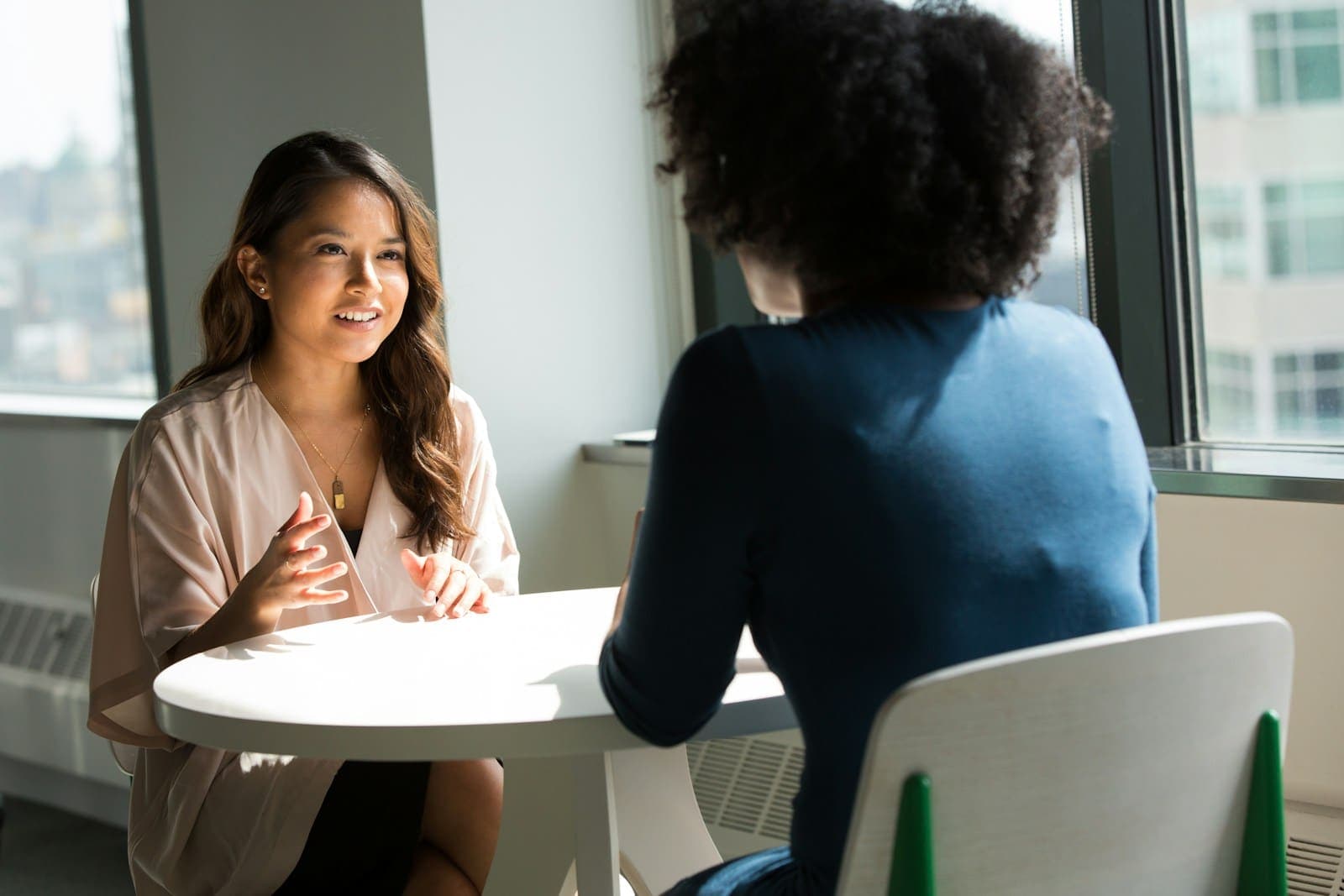 Two professionals talking at a small table by a bright office window